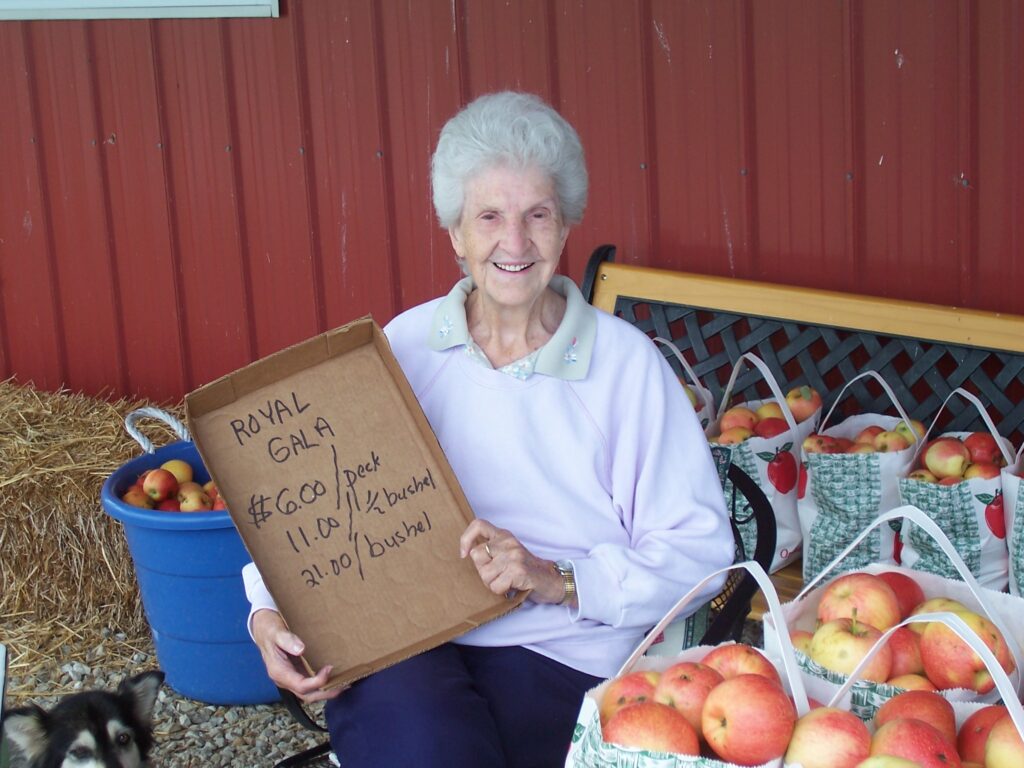 Sallie, holding up a sign in front of produce for sale