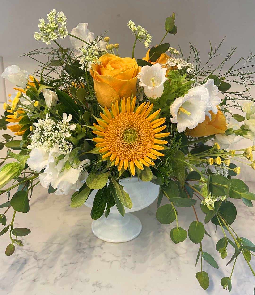 Sun flowers and yellow and white roses mixed in an arrangement in a white glass vase